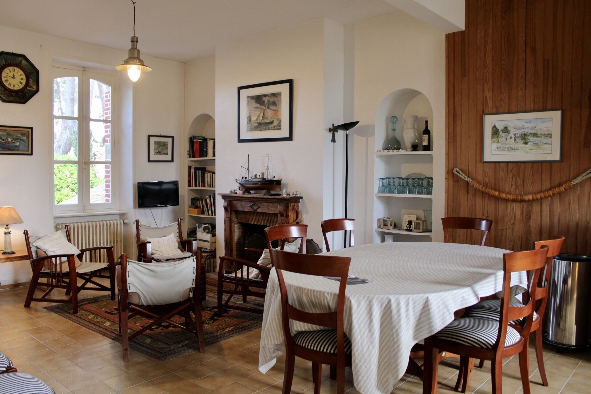 Comedor con mesa redonda, sillas de madera, chimenea, estanterías y obras de arte.