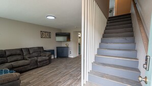Una sala de estar con un sofá modular, un televisor de pantalla plana y una escalera con barandilla de madera.