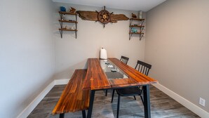 Un comedor con una larga mesa de madera, sillas negras y un adorno con timón de barco en la pared.