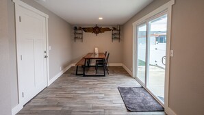 Un pasillo con suelo de madera, una mesa de comedor con sillas, una alfombra y un estante de pared con objetos decorativos.