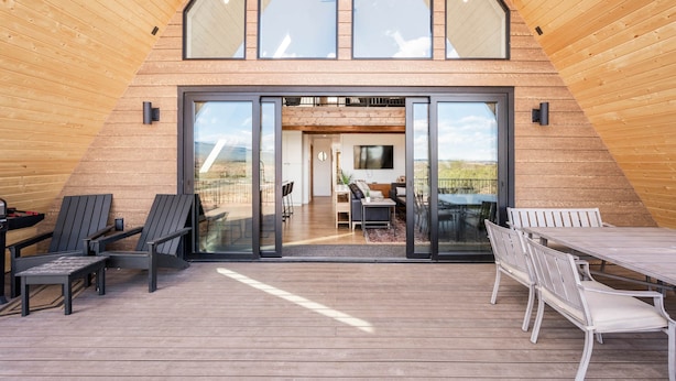 A modern, triangular-roofed building with a glass entrance leading to an interior with a dining area and a TV.
