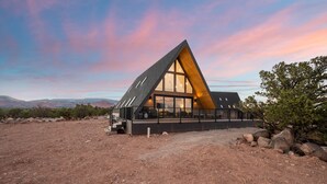 A modern, triangular-shaped building with large windows and a balcony, set in a desert landscape with distant hills.