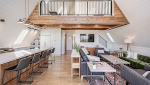 A spacious loft-style living area with a high ceiling, a kitchen with a long counter, and a cozy seating area with a sofa and coffee table.