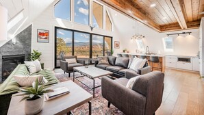 A spacious living room with a fireplace, large windows, and a modern kitchen.