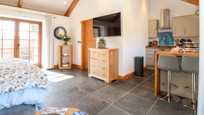 A modern kitchen with a flat-screen TV, wooden cabinets, and a dining area with bar stools. - Rosewarrick Cottage (Bodmin)