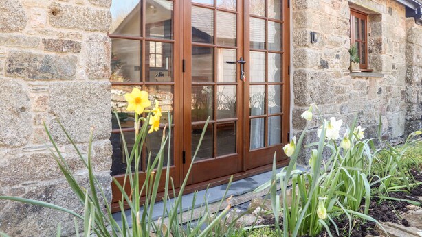 A stone building with a wooden door and windows, surrounded by plants. - Rosewarrick Cottage (Bodmin)