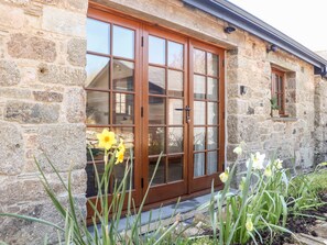 A stone building with a wooden door and windows, surrounded by plants. - Rosewarrick Cottage (Bodmin)