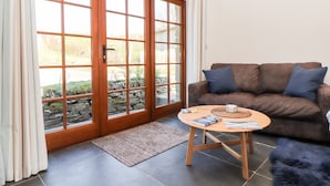 A living room with a brown leather sofa, a wooden coffee table, and a large glass door leading to an outdoor area with stone walls. - Rosewarrick Cottage (Bodmin)