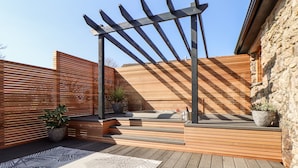 A wooden deck with a pergola, potted plants, and a stone wall. - Rosewarrick Cottage (Bodmin)