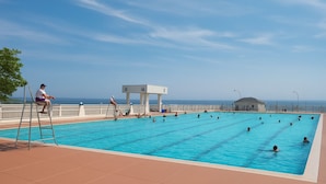 Una piscina con vista al océano, una silla de salvavidas y un pequeño pabellón.