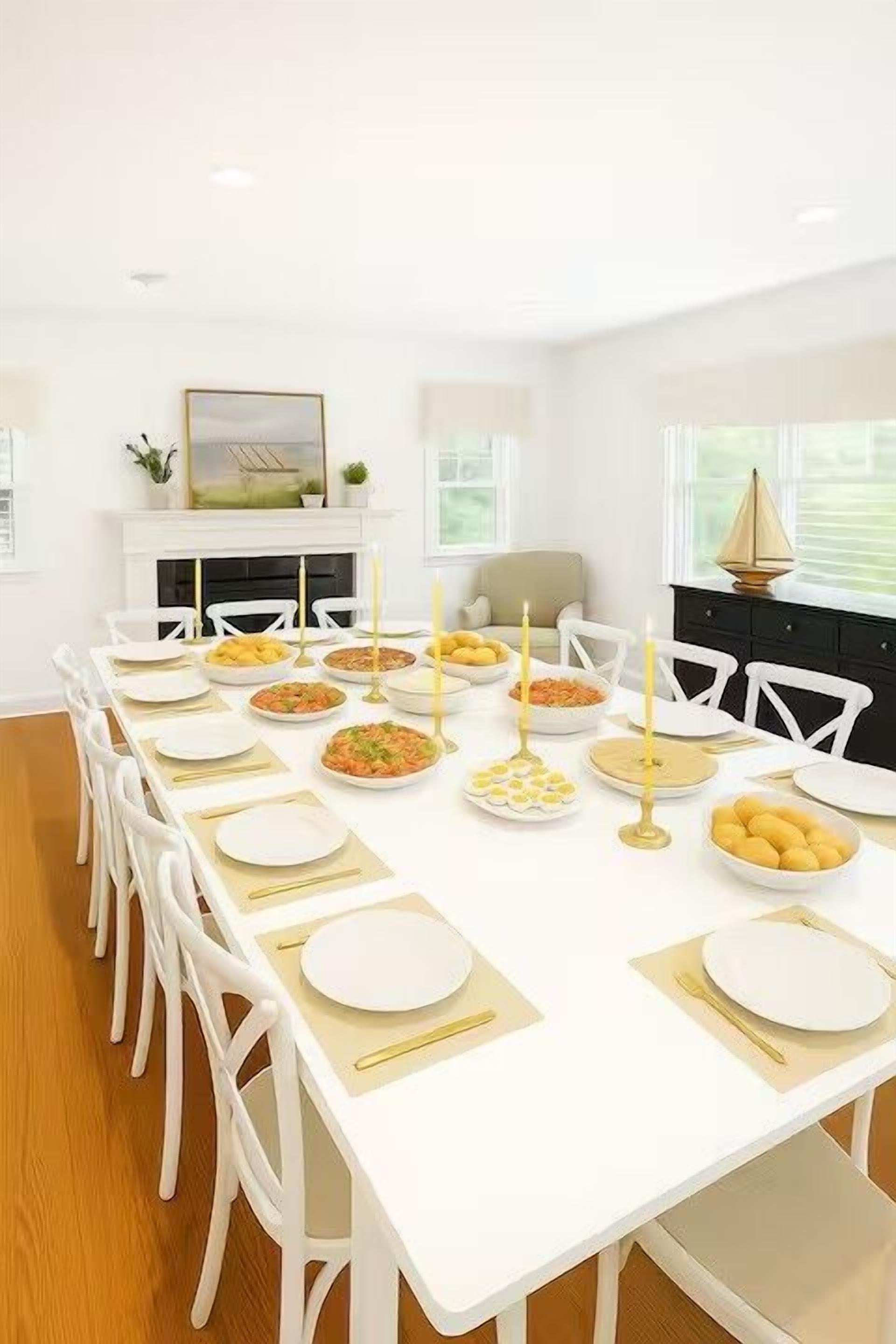 A dining room with a long white table set for a meal, white chairs, and a fireplace in the background.