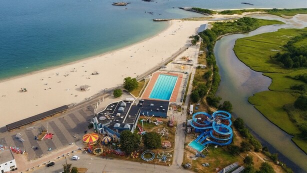 Vista aérea de un complejo turístico con piscina, toboganes acuáticos y aparcamiento.
