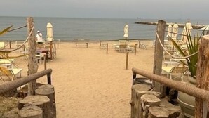 Un escalier en bois mène à une plage où se trouvent des chaises longues et des parasols.