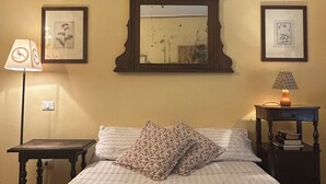 Un lit bien fait, recouvert d’une couverture verte, avec deux oreillers, un miroir au-dessus du lit et deux tableaux encadrés accrochés au mur.
