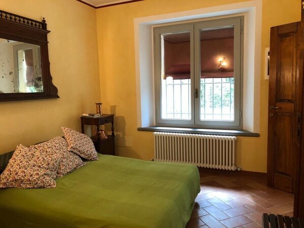 A bedroom with a bed, a window with a view, a radiator, and a wooden door. - Casa del Gallo Ravenna Charme Country House (Sant'Alberto)