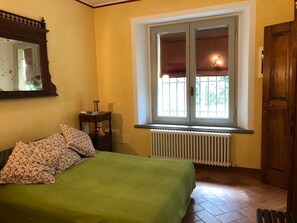 Un dormitorio con cama, ventana con vistas, radiador y puerta de madera.