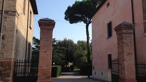 Une cour pavée, avec un bâtiment en briques sur la gauche et un bâtiment rose sur la droite, séparés par un portail.