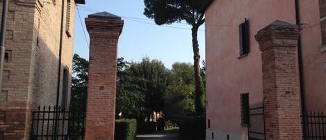 A paved courtyard with a brick building on the left and a pink building on the right, separated by a gate.