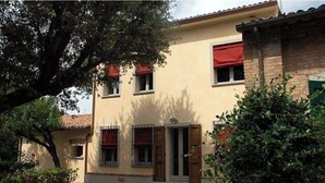 Un bâtiment à deux étages, doté d’une façade beige, de volets rouges et d’un petit porche à l’avant.