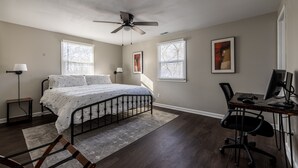 A bedroom with a bed, desk, computer, and ceiling fan.
