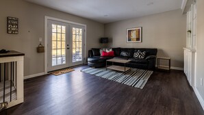 A living room with a dark wood floor, a black leather sofa, a coffee table, and a framed picture on the wall.