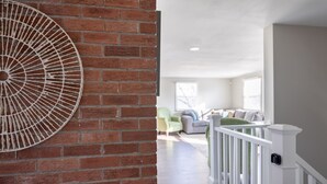 A spacious living area with a brick wall, a white railing, and a large decorative wall piece.