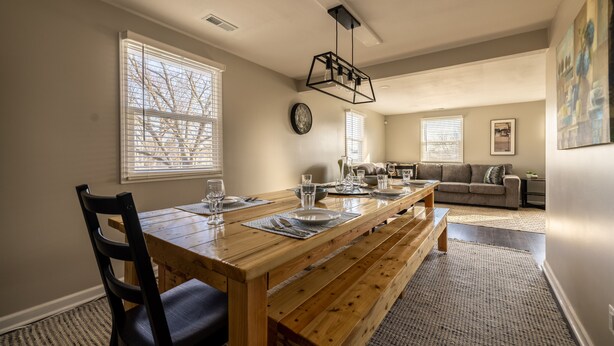 A dining area with a wooden table set for four, a sofa, and a clock on the wall.