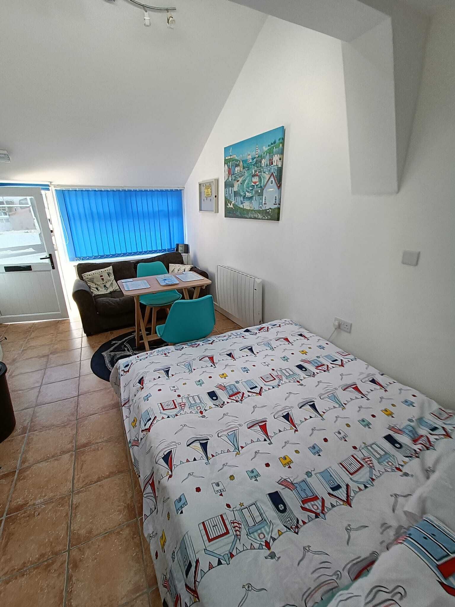 A bedroom with a bed, a desk, a chair, and a window with blinds.