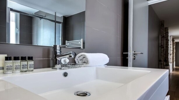 A modern bathroom with a large white sink, a mirror, and a towel rack. - A Bit of Glamour and Magic in Champs Elysees (Paris)