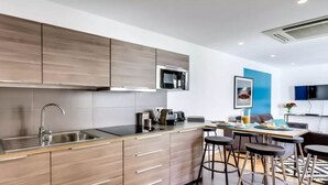 A modern kitchen with a built-in microwave, stainless steel sink, and wooden cabinets. There is a dining area with a table and bar stools. - A Bit of Glamour and Magic in Champs Elysees (Paris)
