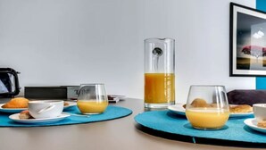 A breakfast setup with a laptop, a tall glass of orange juice, and a cup of coffee on a table with a blue placemat. - A Bit of Glamour and Magic in Champs Elysees (Paris)