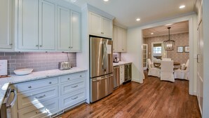 A kitchen with light blue cabinets, a stainless steel refrigerator, and a wooden floor.