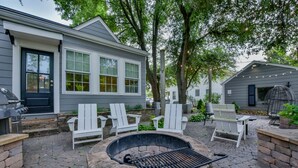 A patio with a stone fire pit, white Adirondack chairs, and a grill.