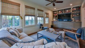 A living room with a sofa, coffee table, and chairs. There is a television and a cabinet in the background.