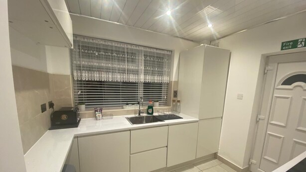 A modern kitchen with white cabinetry, a stainless steel sink, and a window with blinds. - Charming 3-bed House Near Central Manchester (Manchester)