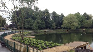A park with a pond, a wooden dock, and a green fence. - Charming 3-bed House Near Central Manchester (Manchester)