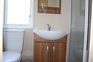 A bathroom with a toilet, a sink with a mirror above it, and a shower area. - Loch View - luxury cabin with spectacular alpine and loch views (Taynuilt)