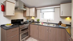 A modern kitchen with a gas stove, oven, and sink. There is a fire extinguisher mounted on the wall, and a window with blinds.