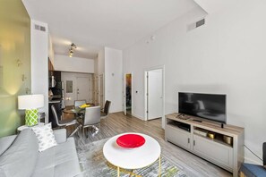 Relax in a comfortable seating area with a sofa and coffee table, featuring a flat-screen TV and dining space with a glass table and chairs.