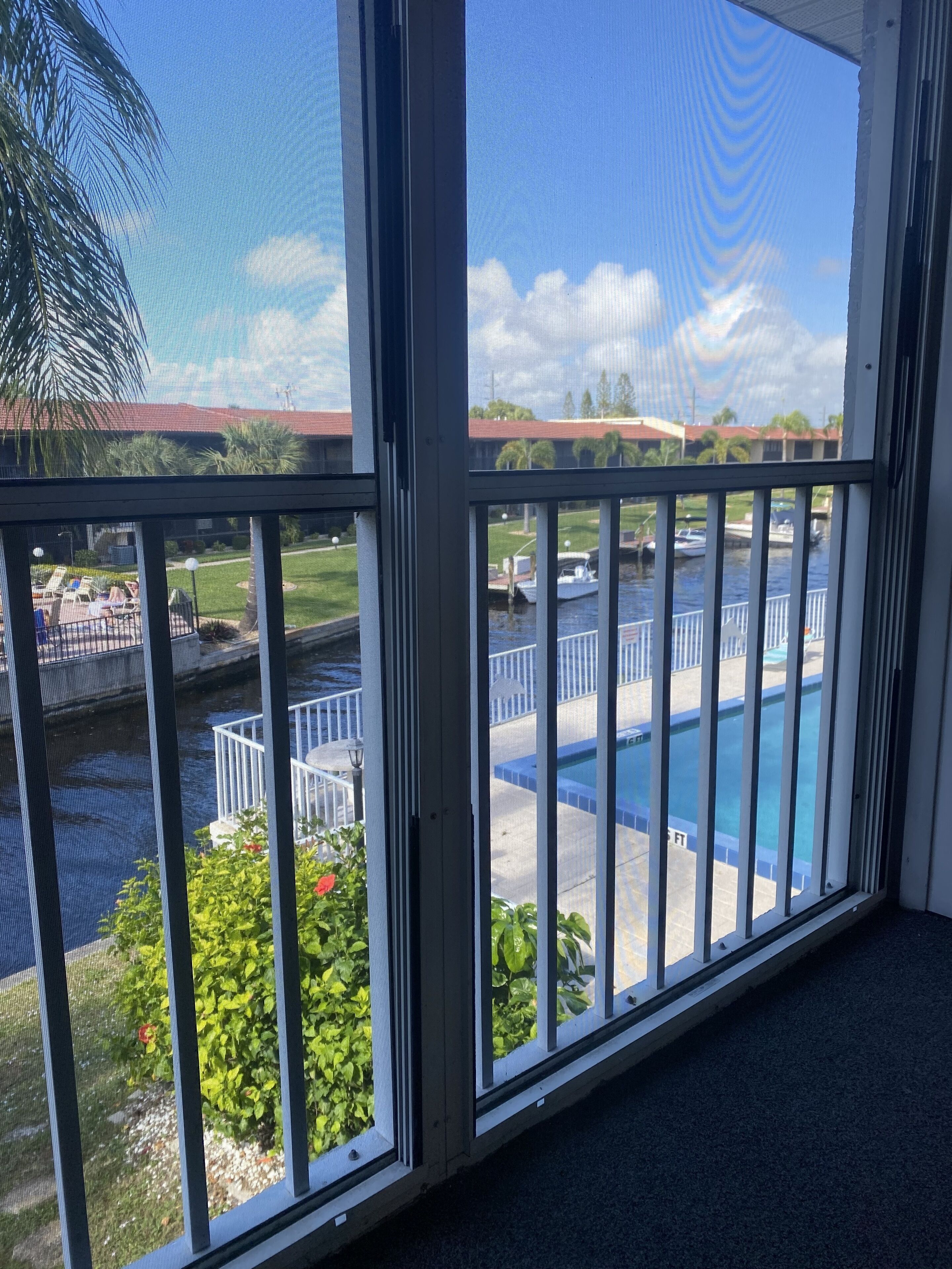 Une vue depuis un balcon donnant sur une piscine, une étendue d’eau et un bâtiment éloigné avec un toit rouge.