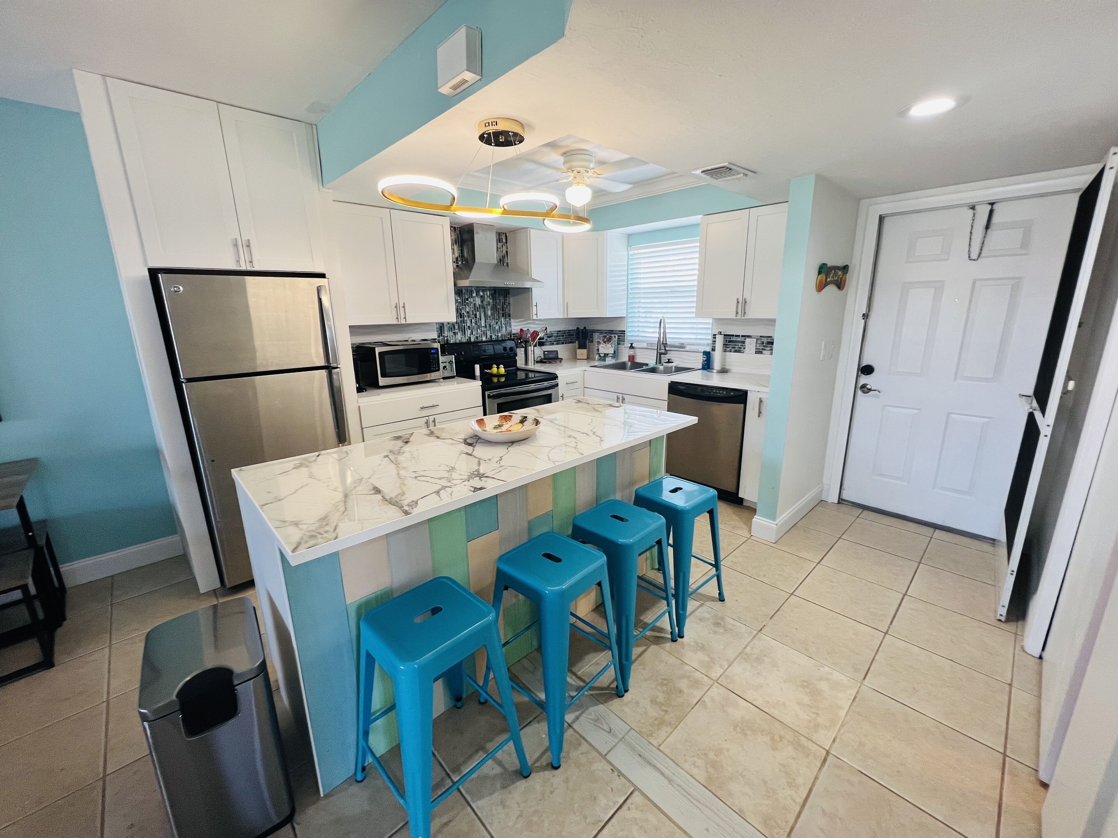 A modern kitchen with a marble countertop, stainless steel appliances, and blue bar stools.