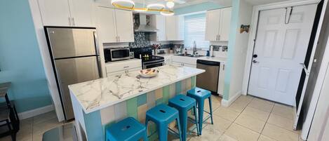 A modern kitchen with a marble countertop, stainless steel appliances, and blue bar stools.
