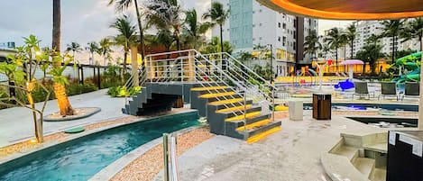A pool area with clear water, palm trees, and a modern building in the background.