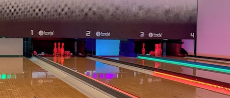 A bowling alley with multiple lanes, wooden flooring, and a modern wall with geometric patterns.