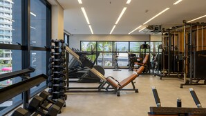 A modern gym with various exercise equipment, large windows, and a view of palm trees. - Premium - GAV Hotéis e Resorts (Salinópolis)