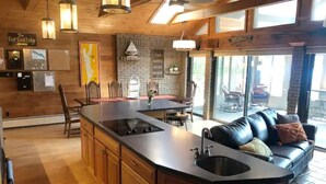 A spacious kitchen with a central island, wooden cabinets, and a dining area with chairs. - “The Lake house” Private BEACH; SLEEPS 16!!! (Schroon Lake)