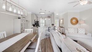 A modern kitchen with white cabinets, a wooden dining table, and pendant lighting. - Snowbird Special Jan Feb! 🌊Canal View~pools~Walk2Beach~2BR Sandpiper Cove 4114 (Destin)