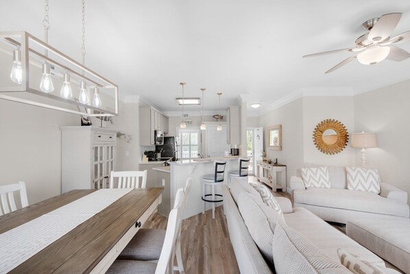 A modern kitchen with white cabinets, a wooden dining table, and pendant lighting.