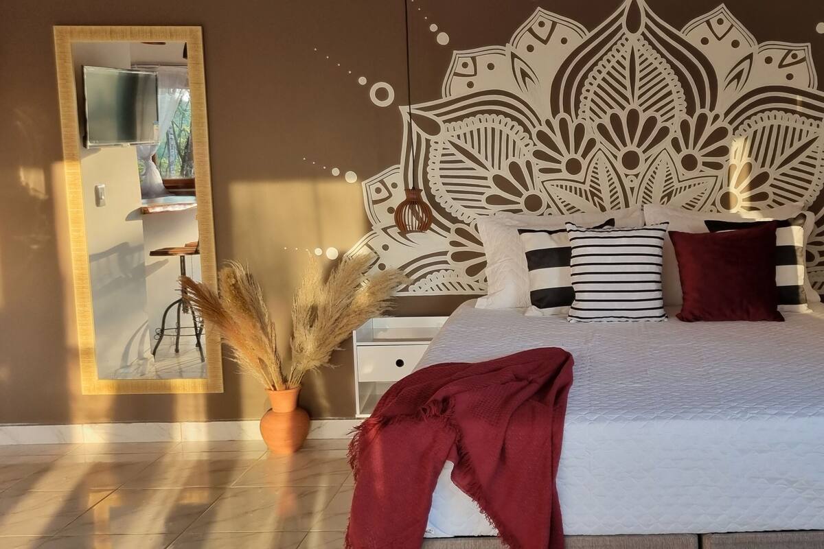 Ein Schlafzimmer mit Bett, Nachttisch, Spiegel und einem dekorativen Wandpaneel.