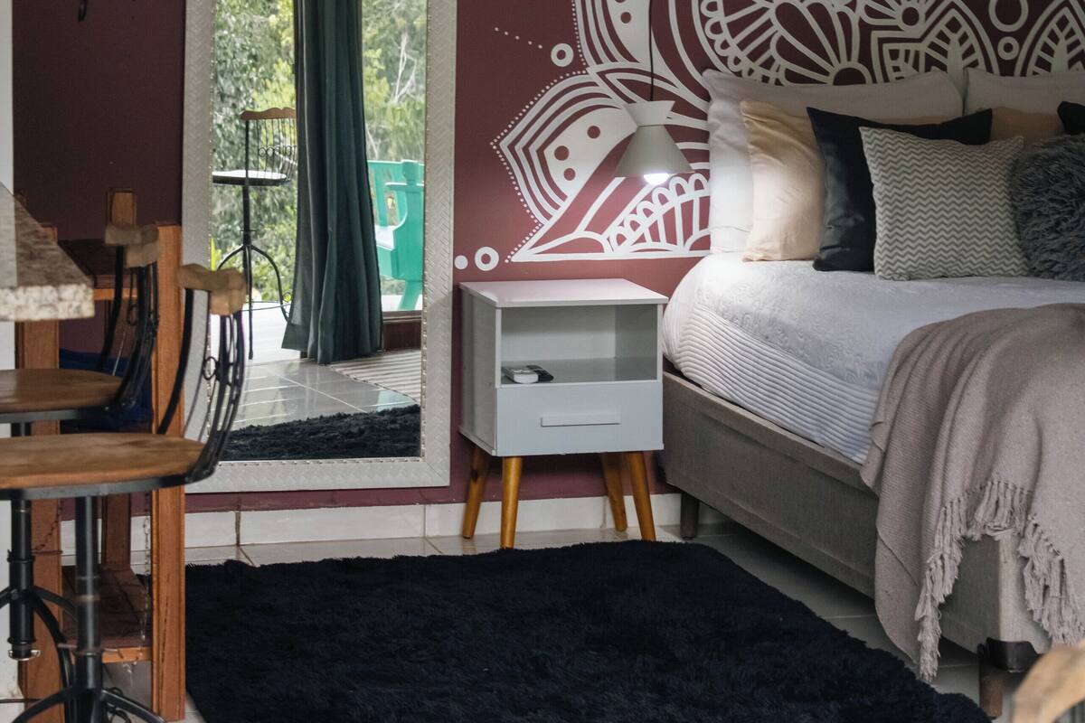Ein Schlafzimmer mit Bett, Nachttisch, Stuhl, Schreibtisch, Fenster mit Blick und einem dekorativen Wandmuster.